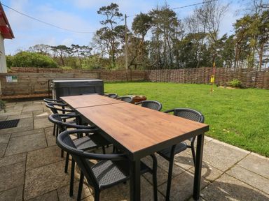 An outdoor patio with a wooden table and black chairs next to a grassy yard with a woven fence at Rempstone Farmhouse in Corfe Castle
