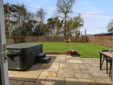 A backyard with a hot tub fire pit grass and a table with chairs at Rempstone Farmhouse in Corfe Castle