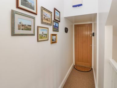 A hallway with a wooden door a semicircular rug and pictures on the wall at Grassholm View in Solva