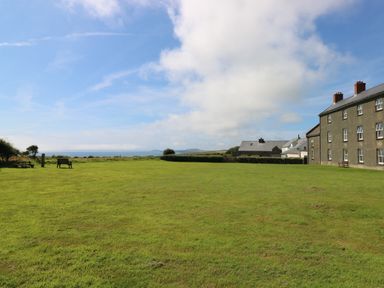 An open grassy field with benches and houses near a coast at Grassholm View in Solva