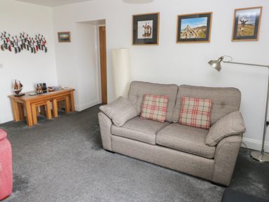 A living room with a grey sofa, a floor lamp, framed pictures on the wall, and nested wooden tables at Grassholm View in Solva