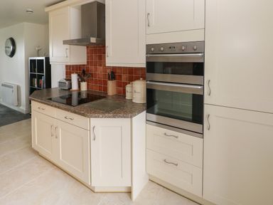 A kitchen with white cabinets a built-in double oven a stovetop under a range hood and kitchen utensils on the counter at Grassholm View in Solva