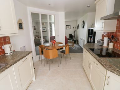 A kitchen with a round dining table and chairs leading to a living room with a sofa and a TV at Grassholm View in Solva