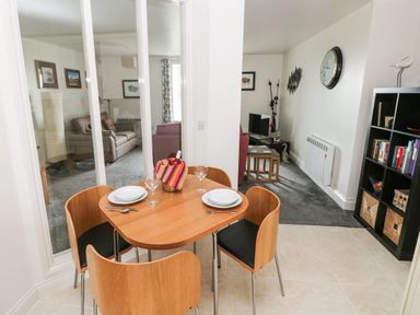 A dining area with a wooden table and four chairs next to a living room with sofas and a TV at Grassholm View in Solva