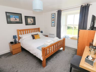 A bedroom with a wooden bed and bedside tables with lamps and a window with curtains at Grassholm View in Solva