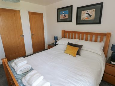 A bedroom with a wooden bed frame white bedding and folded towels on the bed at Grassholm View in Solva