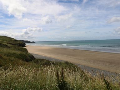 A sandy beach with grassy cliffs and the sea under a cloudy sky at Grassholm View in Solva