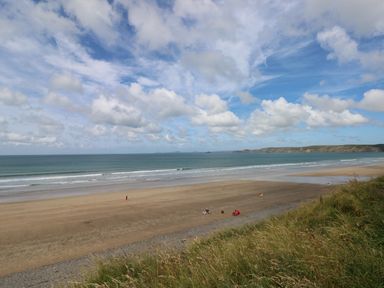 A beach with sand and grassy dunes overlooking the sea under a cloudy sky at Grassholm View in Solva