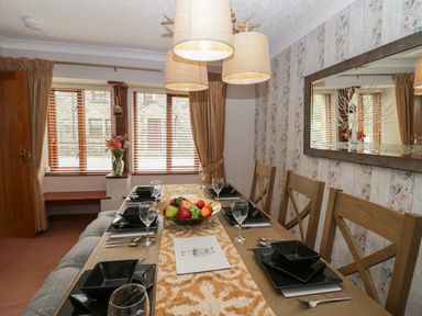 A dining room with a wooden table set with black plates bowls and glasses a fruit bowl and a large mirror on patterned wallpaper at 1 Gilpin House Levens