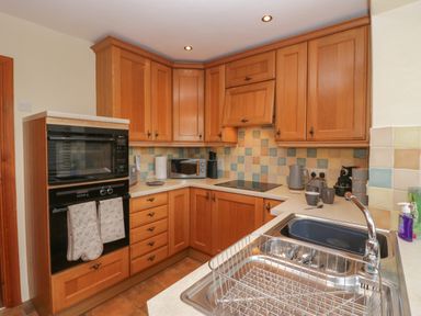A kitchen with wooden cabinets a built in oven a microwave countertop appliances and a stainless steel sink with a drying rack at 1 Gilpin House in Levens