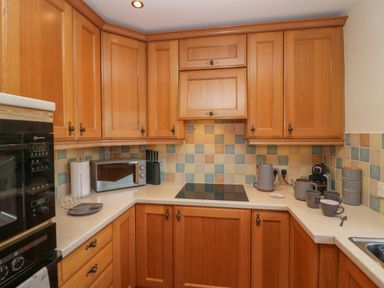 A kitchen with wooden cabinets a microwave electric stove tea set and tiled backsplash at 1 Gilpin House in Levens