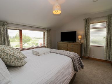 A bedroom with a bed pillows folded towels chest of drawers a television lamp and windows at 1 Gilpin House in Levens