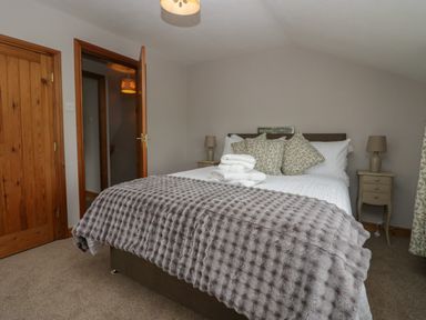 A bedroom with a double bed covered in white bedding and a gray textured throw with bedside tables and lamps at 1 Gilpin House in Levens
