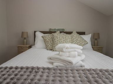 A bed with white linens folded towels and patterned pillows with two bedside tables and lamps at 1 Gilpin House in Levens