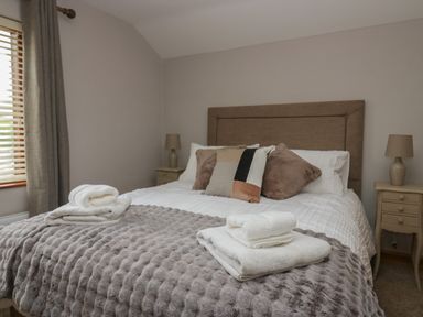 A bedroom with a bed with pillows bedside tables with lamps and folded towels at 1 Gilpin House in Levens