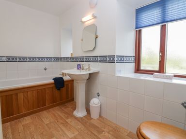 A bathroom with a bathtub a pedestal sink a mirror a window with a blue blind and a wooden toilet seat at 1 Gilpin House in Levens
