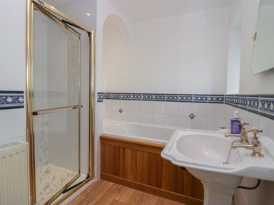 A bathroom with a shower enclosure a bathtub with wooden paneling and a sink with taps at 1 Gilpin House in Levens