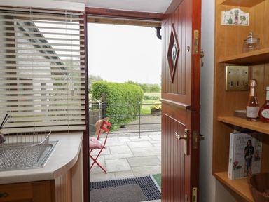 A kitchen door open to a patio with a red chair outside at 1 Gilpin House in Levens