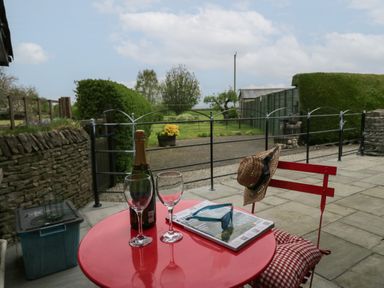 A red table and chair on a stone patio with two glasses a bottle a magazine and sunglasses at 1 Gilpin House in Levens