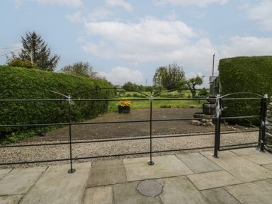 A metal gate with hedges and trees beyond a paved and gravel driveway at 1 Gilpin House in Levens