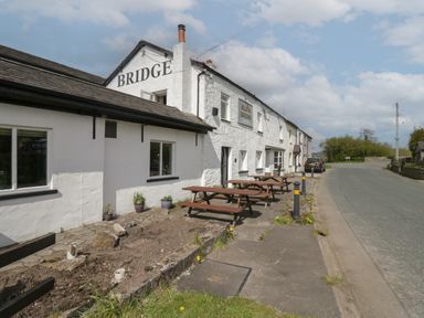A white building with the word bridge on it and picnic tables outside by a road at 1 Gilpin House in Levens