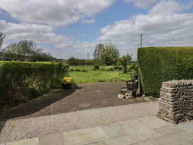 A backyard with a paved patio and stone wall next to a grassy area with bushes and trees at 1 Gilpin House in Levens