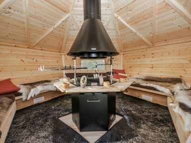 An indoor gathering space with a central fireplace and wooden seating at 1 Gilpin House Levens