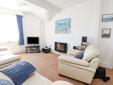 A living room with cream sofas a television and a wall-mounted electric fireplace at Bethan Apartment in Trearddur Bay