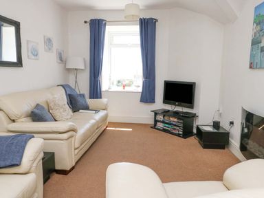 A living room with leather sofas a television on a stand and blue curtains at Bethan Apartment in Trearddur Bay