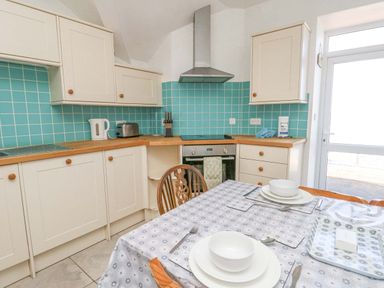A kitchen with cream cabinets turquoise tiled backsplash wooden countertops dining table set with plates and bowls at Bethan Apartment in Trearddur Bay