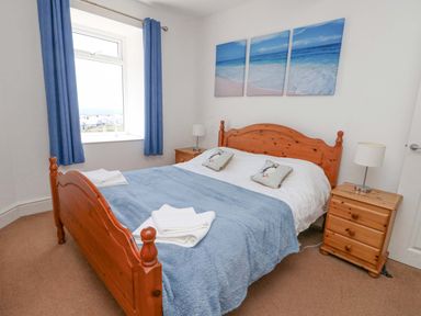 A bedroom with a wooden bed frame blue blanket and matching curtains at Bethan Apartment in Trearddur Bay