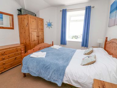 A bedroom with a wooden bed frame blue blanket and matching pillows near a window with blue curtains at Bethan Apartment in Trearddur Bay