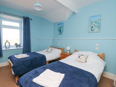 A bedroom with two single beds blue blankets and bird cushions at Bethan Apartment in Trearddur Bay