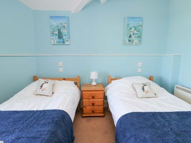 A bedroom with two single beds each with a pillow and navy blue blanket and a wooden nightstand with a lamp between them at Bethan Apartment in Trearddur Bay