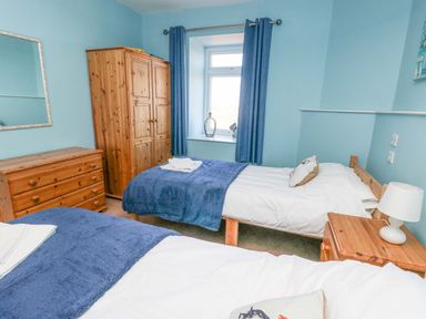 A bedroom with two single beds wooden wardrobe chest of drawers and bedside table with lamp at Bethan Apartment in Trearddur Bay