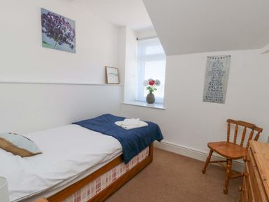 A small bedroom with a single bed a wooden chair and a chest of drawers at Bethan Apartment in Trearddur Bay
