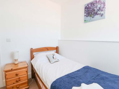 A bedroom with a single wooden bed a wooden bedside table and a lamp at Bethan Apartment in Trearddur Bay