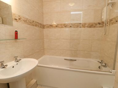 A bathroom with a bathtub sink and tiled walls at Bethan Apartment in Trearddur Bay