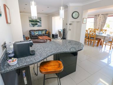 An open kitchen with a granite countertop and wooden stool a living area with sofas and a coffee table and a dining area with a table and chairs at Llain Gwynfor in St Davids