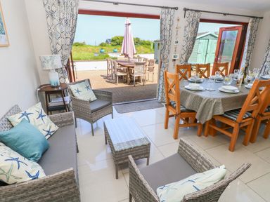 A living and dining room with wicker chairs and table set with plates glasses and cutlery at Llain Gwynfor in St Davids