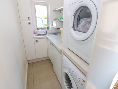A small laundry room with a washing machine, dryer, sink, cabinets, and countertop at Llain Gwynfor in St Davids