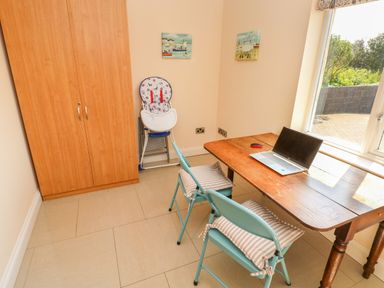 A room with a wooden table and two blue chairs with cushions a laptop on the table a wooden wardrobe a high chair and two paintings on the wall at Llain Gwynfor in St Davids