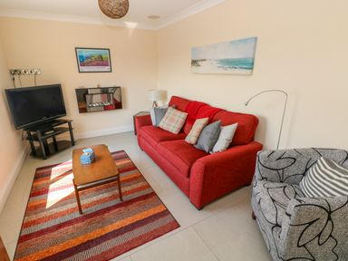 A living room with a red sofa gray patterned armchair wooden coffee table and television at Llain Gwynfor in St Davids