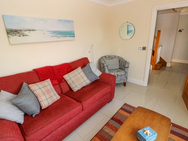 A sitting room with a red couch with cushions a patterned armchair a coffee table and wall art at Llain Gwynfor in St Davids