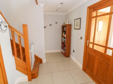 A hallway with wooden stairs a wooden bookshelf and a wooden door at Llain Gwynfor in St Davids