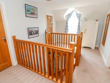 A hallway with wooden stair railings two framed pictures on the wall a white cabinet near a window with blue patterned curtains at Llain Gwynfor in St Davids