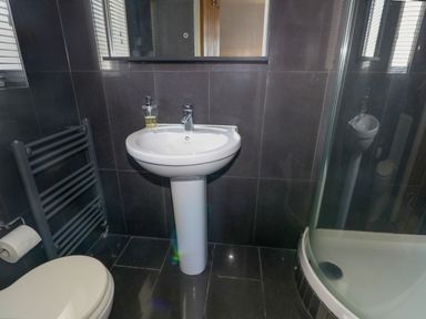 A bathroom with a pedestal sink soap dispenser toilet paper holder towel radiator and a curved glass shower enclosure at Llain Gwynfor in St Davids