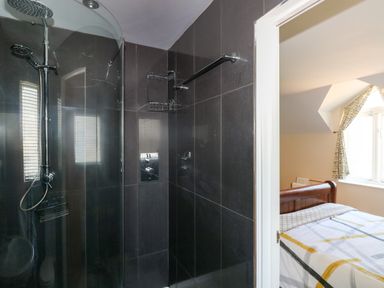 A bathroom with a shower next to a bedroom with a bed and patterned curtains at Llain Gwynfor in St Davids