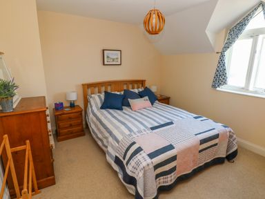 A bedroom with a bed with striped bedding and multiple pillows two wooden nightstands with lamps a wooden chest of drawers and a window with patterned curtains at Llain Gwynfor in St Davids