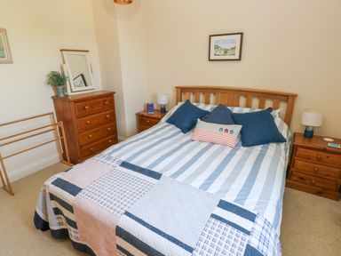A bedroom with a double bed with blue and white bedding and three cushions two wooden bedside tables each with a lamp and a wooden chest of drawers with a mirror and a potted plant at Llain Gwynfor in St Davids